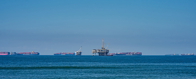 A line of cargo ships wait in line to dock in port along the California coast