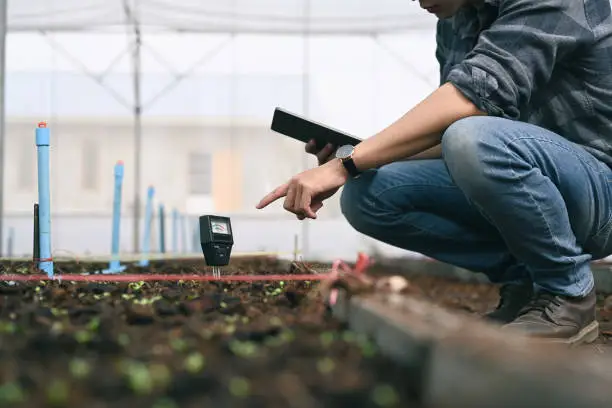 Photo of Smart young asian agronomist man measure soil with digital device and tablet. Technology in the agriculture.