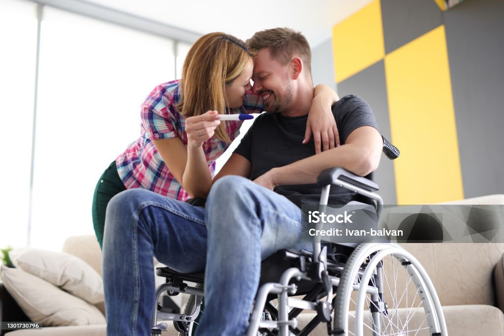 Joyful woman and man in wheelchair with pregnancy test Joyful woman and man in wheelchair with pregnancy test. First emotions of future parents concept Couple - Relationship Stock Photo