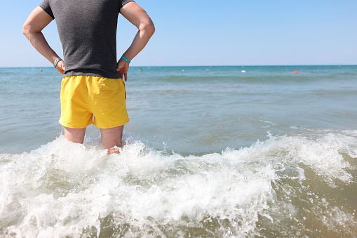 Man in yellow shorts stands knee-deep in sea. Lifeguard work at sea concept