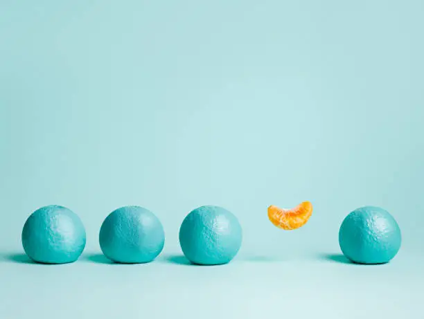 Photo of Creative pattern made of outstanding levitating orange slice surrounded by blue colored oranges on blue background