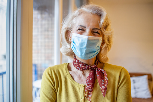 Photo of woman wearing a protective face mask at home. She is smiling and looking at camera