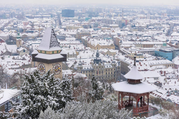 the famous clock tower on schlossberg hill and historic buildings rooftops with snow, in graz, styria region, austria, in winter day - graz austria clock tower styria imagens e fotografias de stock