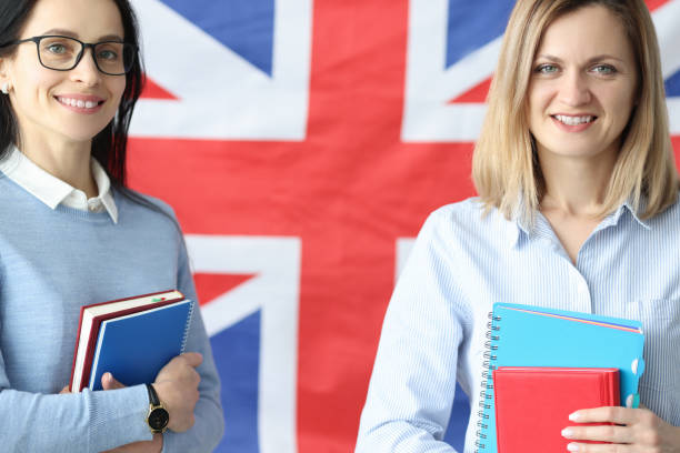 istock Two smiling women stand with notebooks in front of British flag 1301743122