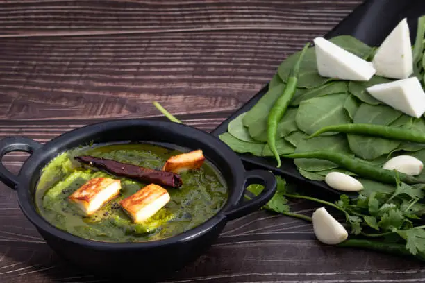 Photo of Most Enjoyed Traditional Indian Palak Paneer Ki Sabji Or Paalak Panir Ki Sabzi Made Of Thick Gravy Of Fresh Spinach Mixed With Spices Herbs And Roasted Cottage Cheese. Wooden Background And Copy Space