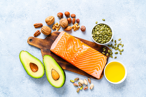 Healthy eating for well balanced diet and heart care: overhead view of a group of food rich in healthy fats. The composition includes salmon, avocado, extra virgin olive oil, nuts and seeds like walnut, almonds, pecan, hazelnuts, pistachio and pumpkin seeds. High resolution 42Mp studio digital capture taken with SONY A7rII and Zeiss Batis 40mm F2.0 CF lens