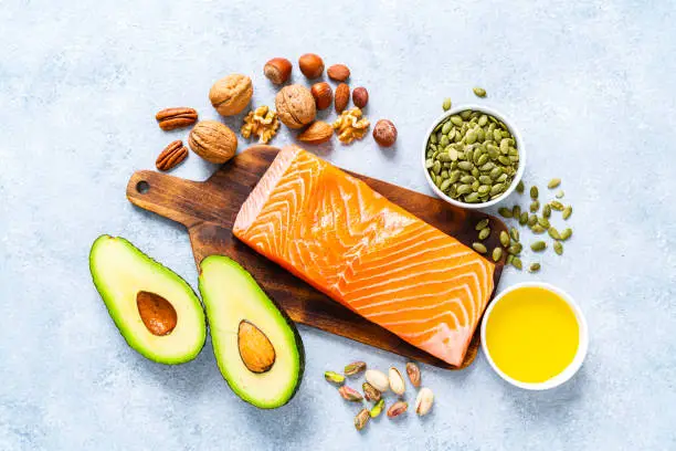 Healthy eating for well balanced diet and heart care: overhead view of a group of food rich in healthy fats. The composition includes salmon, avocado, extra virgin olive oil, nuts and seeds like walnut, almonds, pecan, hazelnuts, pistachio and pumpkin seeds. High resolution 42Mp studio digital capture taken with SONY A7rII and Zeiss Batis 40mm F2.0 CF lens