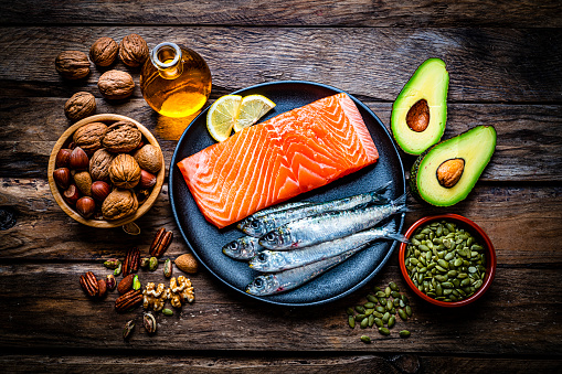Healthy eating for well balanced diet and heart care: overhead view of a group of food rich in healthy fats shot on rustic wooden table. The composition includes salmon, sardines, avocado, extra virgin olive oil, nuts and seeds like walnut, almonds, pecan, hazelnuts, pistachio and pumpkin seeds. High resolution 42Mp studio digital capture taken with SONY A7rII and Zeiss Batis 40mm F2.0 CF lens