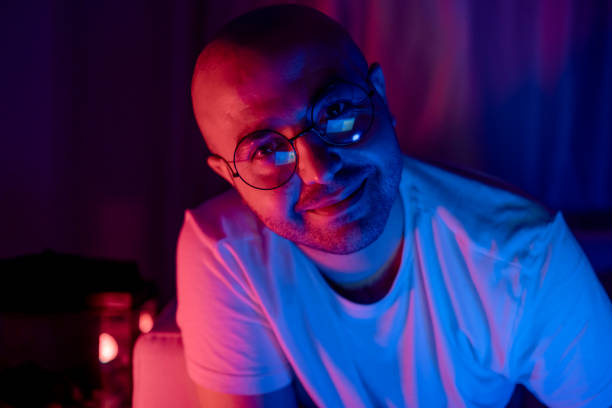istock bald and glasses young man looking at camera in blue and red neon light room smiling 1301751355