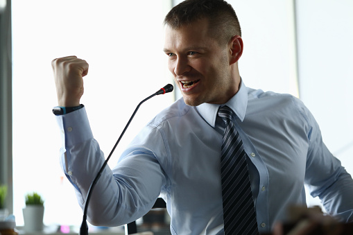 Portrait of confident man in presentable suit public speaking with strong speech. Businessman showing fist as symbol of win. Male formally-dressed on conference room