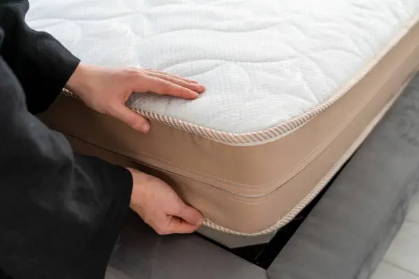 Cropped view of woman choosing bed in store. Female hand on orthopedic memory foam mattress with comfortable and soft white topper. Concept of consumer and purchase