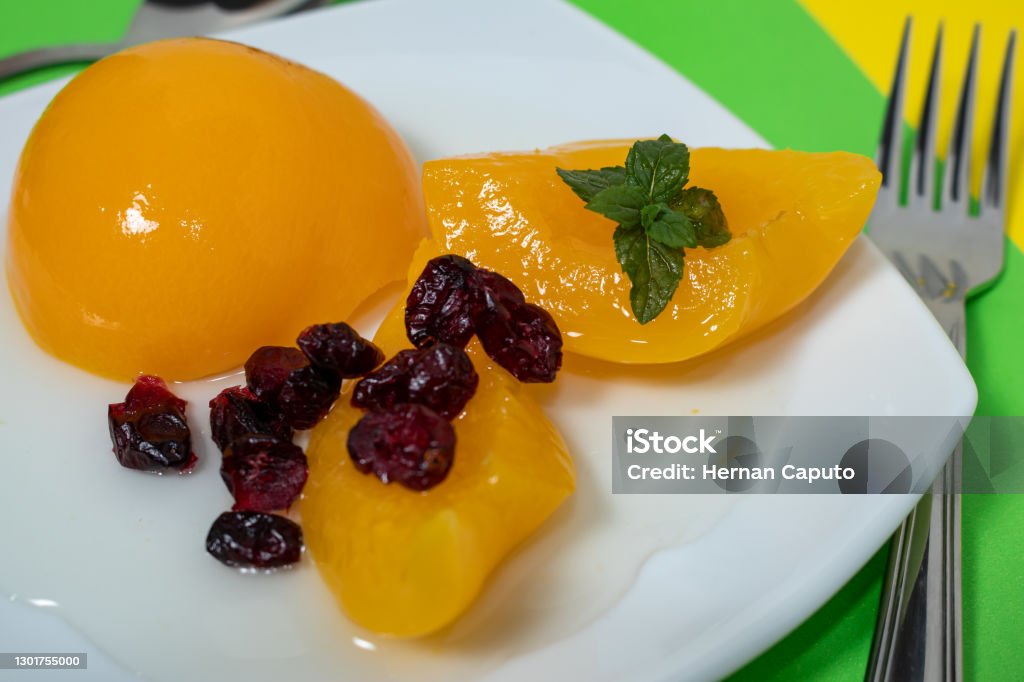 delicious peaches in syrup in a glass bowl on a colored surface and some cranberries. delicious peaches in syrup in a glass bowl on a colored surface and some cranberries. Concept healty food. Apricot Stock Photo