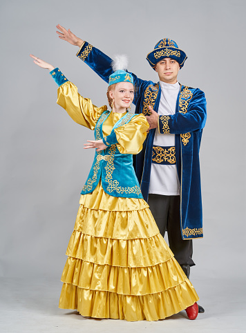 Two dancers (teenage girl and young man) are dressed in a Kazakh traditional clothing. The dancers are dancing Kazakh folk dance and showing traditional poses. They are smiling looking at the camera. Studio shooting