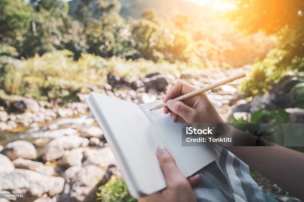 Woman hand writing on notebook with pencil at river background. Diary Stock Photo