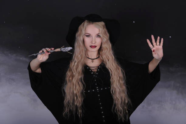 istock Beautiful woman in hat with magic wand on dak background. 1301760074