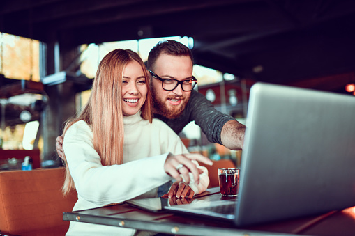 Smiling Female Pointing At Funny Picture On Laptop While Laughing With Boyfriend
