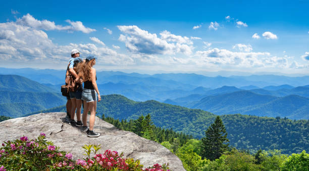 Family on top of the mountain enjoying beautiful view. Family standing with arms around on top of the mountain, looking at beautiful summer mountains landscape. People hiking on vacation, enjoying beautiful view. Great Smoky Mountains in the background. Near Asheaville, North Carolina, USA. blue ridge parkway stock pictures, royalty-free photos & images