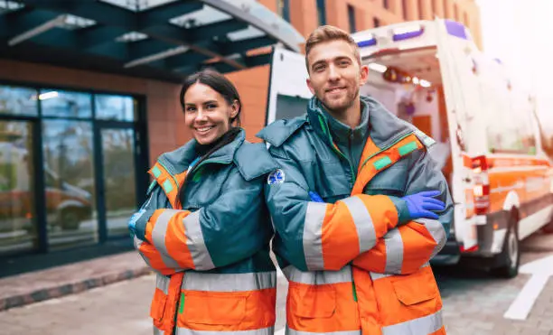 Photo of Two confident young doctors looking on the camera on ambulance and hospital background