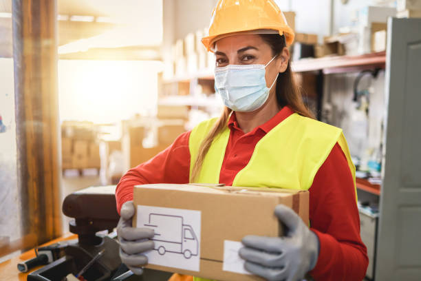 istock Hispanic warehouse worker woman holding delivery box while wearing safety mask - Focus on face 1301768574