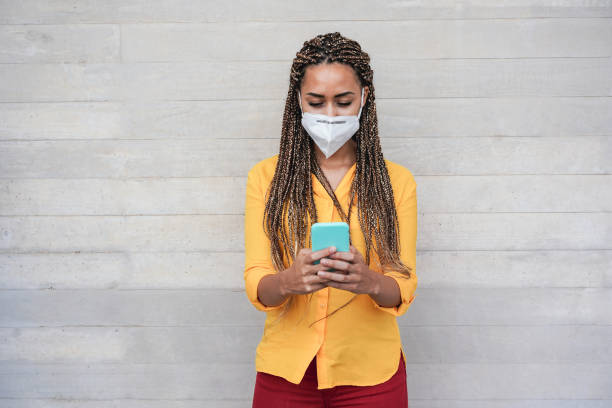 istock Happy african woman with protective face mask using mobile phone outdoors - Focus on face 1301768603