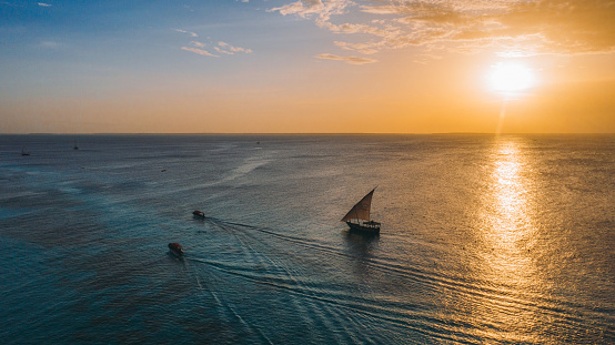 Drone panoramic photo of three sailing boats above the Indian Ocean with view of the colorful sunny sunset on the tropical island of Zanzibar