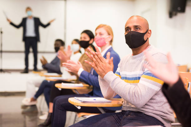 istock Hispanic man in protective mask applauding during business seminar 1301773052