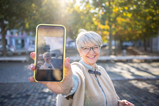 Beautiful senior woman showing her selfie on her mobile phone. Mature woman with short gray hair in the city.