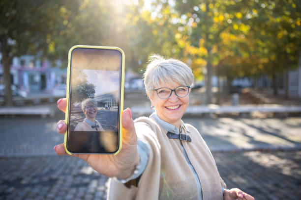 Beautiful senior woman showing her selfie Beautiful senior woman showing her selfie on her mobile phone. Mature woman with short gray hair in the city. women taking selfies photos stock pictures, royalty-free photos & images