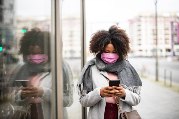 istock African female with face mask walking in city using phone 1301773372
