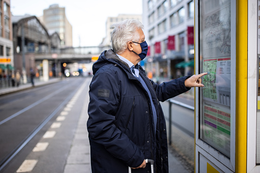 Senior man in face mask looking at the bus line on map