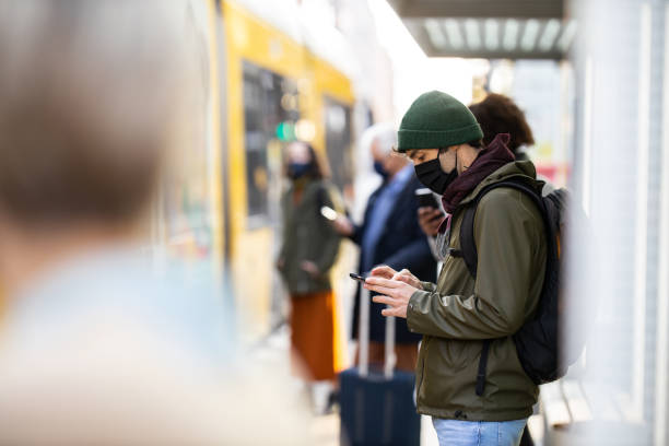 Young man waiting at city tram station during pandemic Young man wearing face mask standing at the crowded tram station. People wearing protective face masks standing at city transport station during coronavirus pandemic. covid crowd stock pictures, royalty-free photos & images