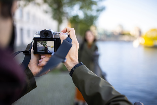 Cropped image of man photographing female friend through digital camera. Female tourist seen on device screen, couple taking pictures on their weekend trip.