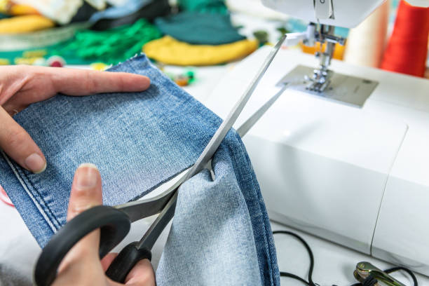 istock Scissors cutting jeans. A dressmaker's workspace. Table with sewing machine and sewing tools. 1301776616