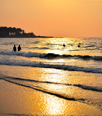People playing silhouette at the beach during evening time. Sunlight shines golden the sea water with beach.
