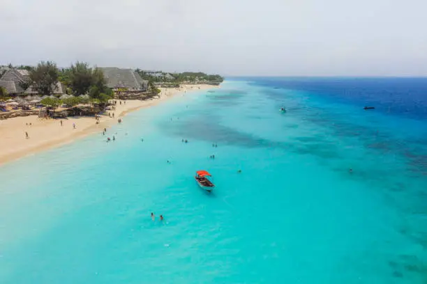 Drone panoramic photo of the Nungwi beach on tropical island of Zanzibar with. old red sailboat, people swimming in the pure blue Indian Ocean and tourist resorts during sunny summer day