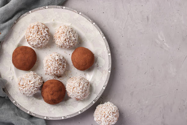 bolas energéticas de frutos secos y avena con copos de coco y cacao sobre plato blanco sobre fondo gris, formato horizontal - peanut bowl nut circle fotografías e imágenes de stock