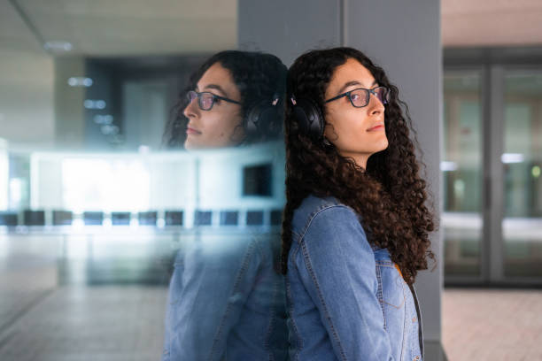 Transgender woman with afro hair sitting and leaning against a window and her reflection. stock photo