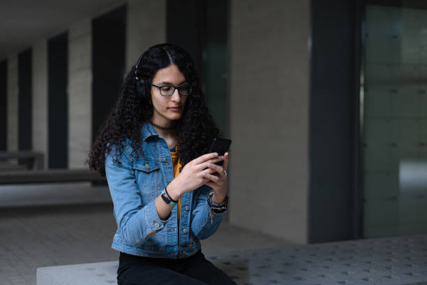 Transgender student with afro hair sitting on a bench while checking her cell phone stock photo