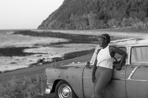 Black and white photography of young woman with a vintage car near the beach Travel contemplation in summer collectors car photos stock pictures, royalty-free photos & images
