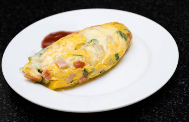 istock Omelet with cheese ham and vegetables. Serving with tomato sauce on white plate. Traditional breakfast of English style or American style 1301791580