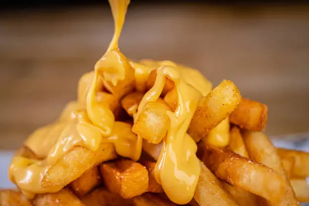 Cheese being poured onto fried French fries.