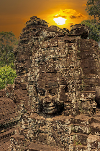 Smiling Buddha face at Bayon Temple against the background of the setting golden sun. Angkor Wat complex in Siem Reap city, Cambodia.