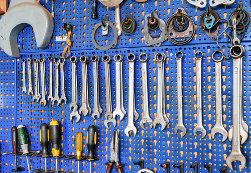 A range of used mechanic tools, from combination wrenches to plier and screwdrivers. All hanging on blue panels. Perfect shot for arts and crafts.