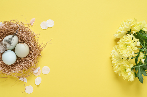 A spring bouquet, yellow little chickens in a large egg and Easter eggs with a golden pattern on the table. In the background is a white Scandinavian-style kitchen. Easter decor in the house.