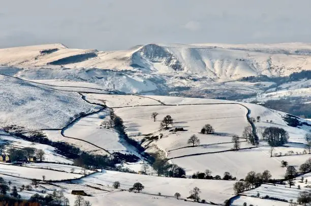 Mam Tor mountain ridge in snow with village of Hathersage in valley