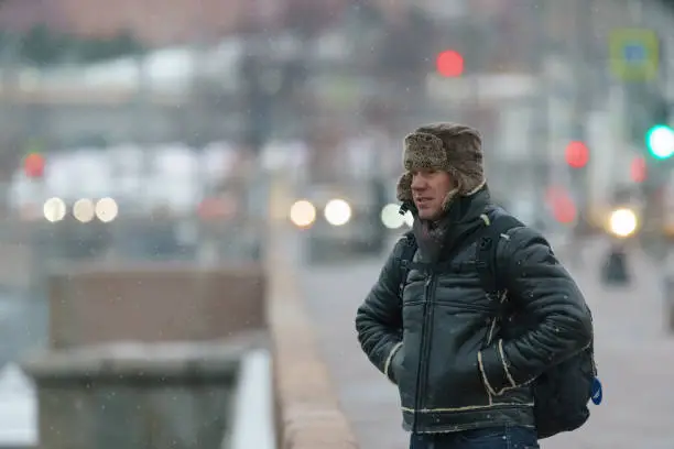 Handsome man walking in Moscow city center. Cold winter in the Russian capital during coronavirus pandemic time. He wear hot cap made of natural sheepskin. It fastened at the chin to protect from cold