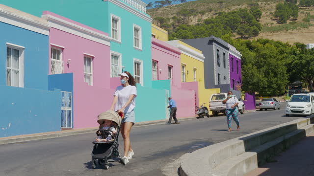Woman walking with baby stroller in the streets of colorful buildings neighbourhood Bo-Kaap Cape Town South Africa.