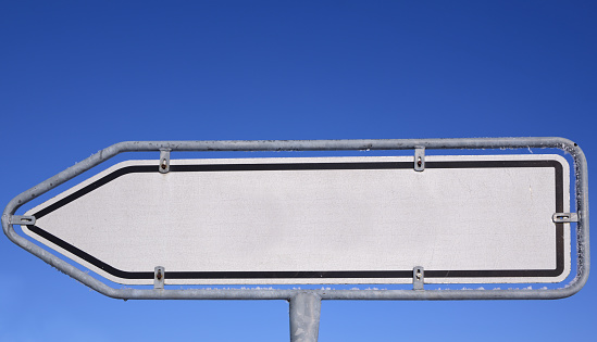 A white weathered sign against a blue sky in the shape of an arrow with space for text