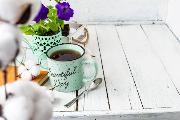 Close-up of a cup of tea on a wooden white table with blurred background, front blur. Still life with flower, book, teaspoon, cotton box. Spring breakfast. Copy space. Close-up of a cup of tea on a wooden white table with blurred background, front blur. Still life with flower, book, teaspoon, cotton box. Spring breakfast. Copy space tea party horizontal nobody indoors stock pictures, royalty-free photos & images