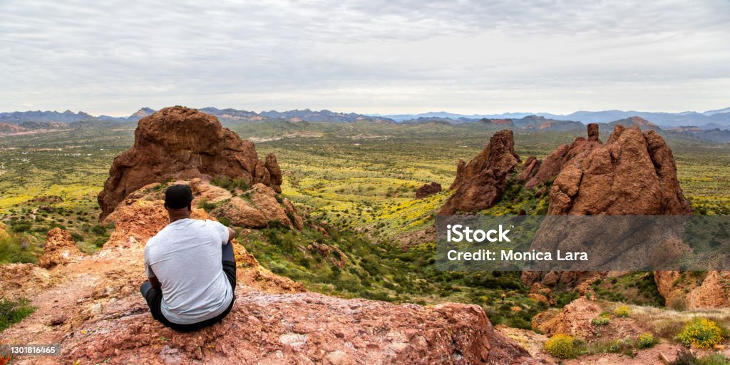 African American Man Looking at Arizona Desert from Flatiron Peak Panorama Black man contemplating the view from The Flatiron in the Superstition Mountains from the basin at the top of Treasure Loop Trail. Hiking in the Arizona desert panoramic. Moutain peak hike banner. Hiking Stock Photo